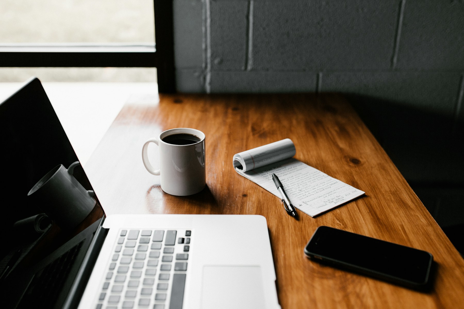 Notebook, coffee, laptop, and phone on a wooden desk